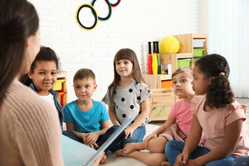 Kindergarten teacher reading book to cute little children indoors