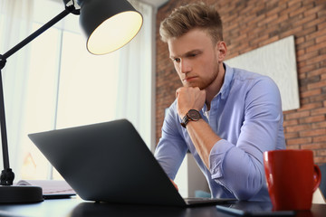 Young man using laptop at table indoors