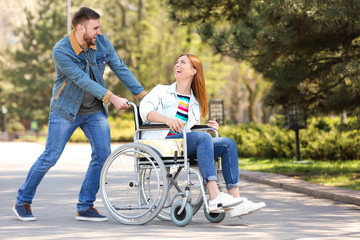 Happy woman in wheelchair and young man at park on sunny day