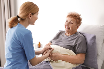 Nurse assisting elderly woman in bed indoors