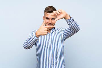 Young handsome blonde man over isolated blue background focusing face. Framing symbol