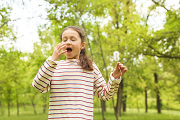 Little girl with dandelions suffering from seasonal allergy outdoors on sunny day