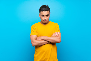 Young man with yellow shirt over isolated blue background feeling upset