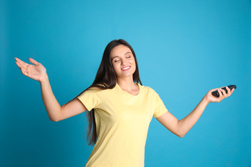 Fototapeta premium Happy young woman with air conditioner remote control on light blue background