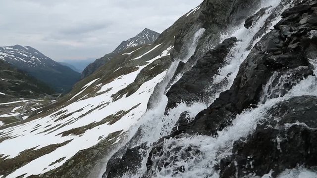 Beautiful waterfal near the Susch pass near Davos in Swizerland surrounded by snow. Filmed in slowmotion in June.