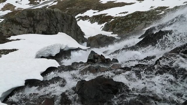 View to the valley and waterfal from mountain near the Susch pass near Davos in Swizerland surrounded by snow. Filmed in slow motion in June.