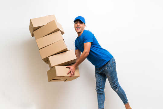 Delivery man over isolated white wall with lots boxes and stumbling