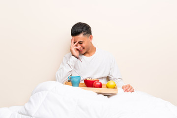 Young man having breakfast in bed laughing