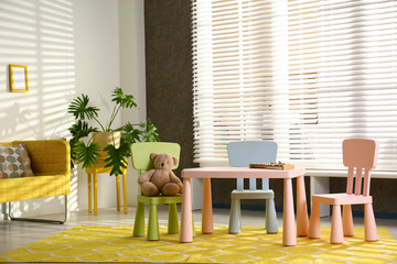 Stylish playroom interior with table, chairs and sofa