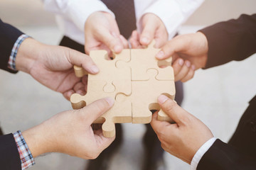 three businessman hand hold trying to connect Jigsaw wooden puzzle piece stand floor office...