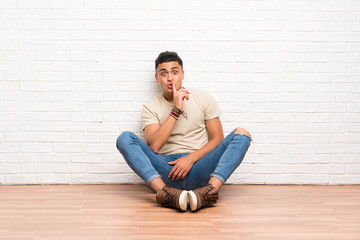 Fototapeta na wymiar Young man sitting on the floor doing silence gesture