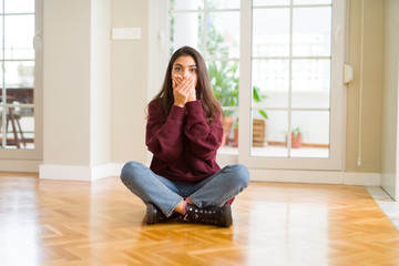 Young beautiful woman sitting on the floor at home shocked covering mouth with hands for mistake. Secret concept.