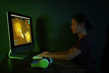 Happy young woman with headphones playing video game in dark room