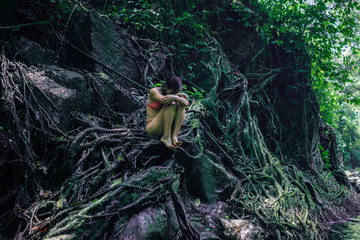 beautiful woman at tropical enchanted forest . Young attractive girl in bikini sitting vulnerable and mysterious on tree trunk at tropical paradise jungle with magical feeling