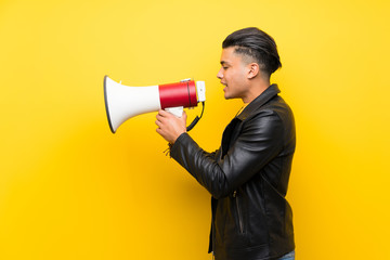 Young man over isolated yellow background shouting through a megaphone