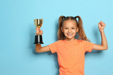 Happy girl with golden winning cup on blue background