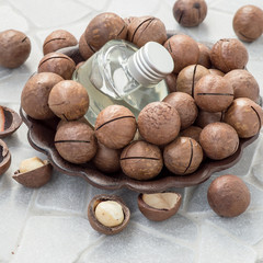 Ripe macadamia nuts and a glass bottle with natural oil on a round brown dish. Source of natural vitamins and minerals. Selective focus.