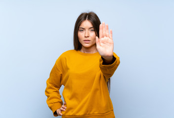 Caucasian young woman over isolated blue wall making stop gesture with her hand - obrazy, fototapety, plakaty