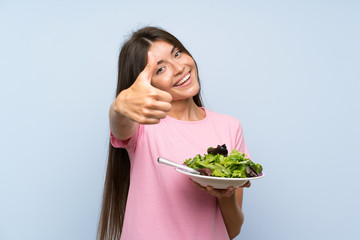 Young woman with salad over isolated blue background with thumbs up because something good has happened