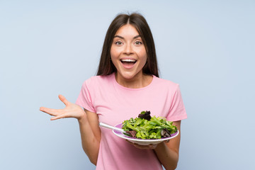 Young woman with salad over isolated blue background with shocked facial expression