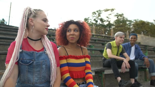 Two female students looking with interest at male classmates sitting outdoors