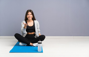 Fototapeta premium Young sport woman sitting on the floor with mat handshaking after good deal
