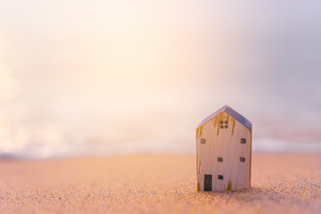Small home model on sunset beach sand texture background.