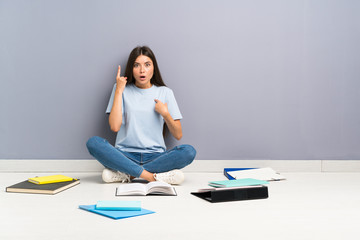 Young student woman with many books on the floor with surprise facial expression