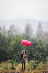 Enjoyment of nature in mist forest. Woman with red umbrella standing in fog and rain