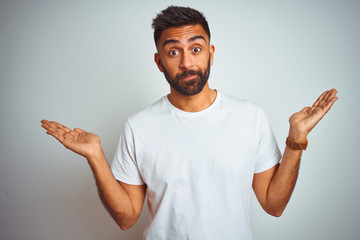 Young indian man wearing t-shirt standing over isolated white background clueless and confused...