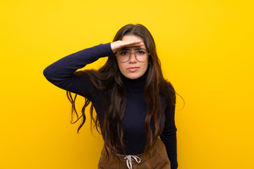 Teenager girl over isolated yellow wall looking far away with hand to look something