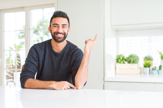 Handsome hispanic man wearing casual sweater at home with a big smile on face, pointing with hand and finger to the side looking at the camera.