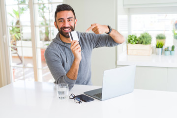 Handsome man smiling using credit card as payment metod when shopping online using laptop