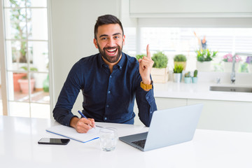 Handsome hispanic man working using computer and writing on a paper surprised with an idea or question pointing finger with happy face, number one