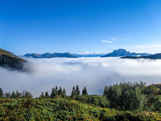 A panoramic view on Alpine valley. The valley is shrouded in dense fog, only tall mountain peaks are visible. Hiking trails in the high mountain. Endless chains of mountains visible. Magical mist.