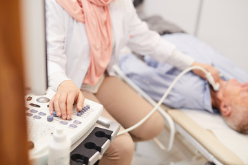 Closeup of unrecognizable female doctor using ultrasound machine while examining senior patient in clinic, copy space