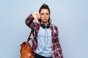Teenager student girl over isolated blue wall showing thumb down with negative expression