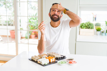 Handsome hispanic man eating asian sushi using chopsticks stressed with hand on head, shocked with shame and surprise face, angry and frustrated. Fear and upset for mistake.