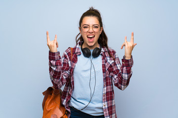 Teenager student girl over isolated blue wall making rock gesture