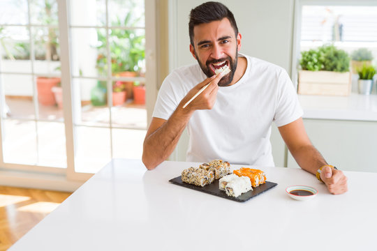 Handsome man smiling happy enjoying eating fresh colorful asian sushi using chopsticks