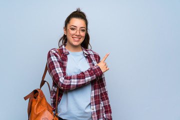 Teenager student girl over isolated blue wall pointing to the side to present a product