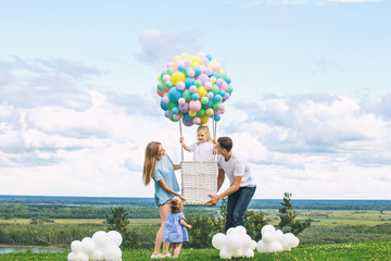 Family mother, father and two daughters beautiful and happy on the green grass with a balloon airship on the background of blue sky with clouds