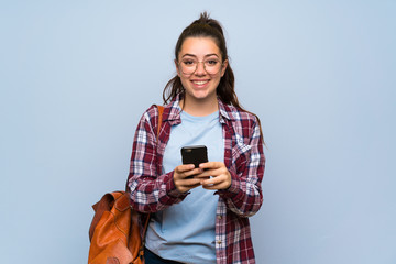 Teenager student girl over isolated blue wall sending a message with the mobile