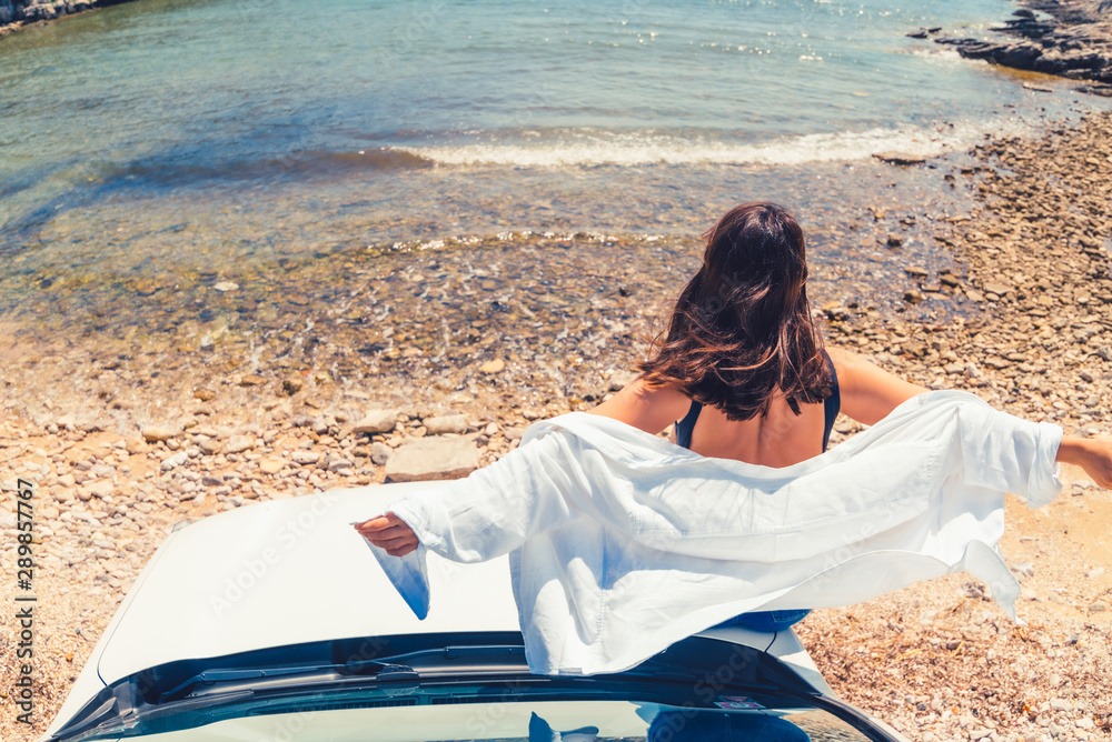 Wall mural woman laying at car hood with view of sea summer beach