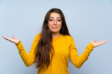 Teenager girl over isolated blue wall having doubts with confuse face expression