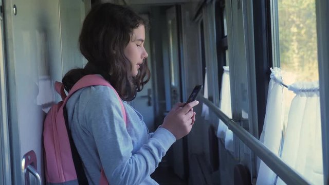 little girl walks on a train compartment car with a backpack and a smartphone. travel transportation railroad concept. the girl in the train at the window corresponds the girl in the train lifestyle