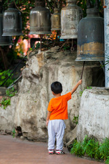 Mały tajski chłopiec uderza w modlitewny dzwon w buddyjskiej świątyni w Bangkoku, jest odwrócony tyłem - obrazy, fototapety, plakaty
