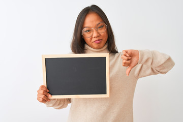 Young chinese woman wearing glasses holding blackboard over isolated white background with angry face, negative sign showing dislike with thumbs down, rejection concept