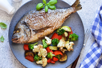 Baked dorado with vegetables and rosemary on a beautiful plate.