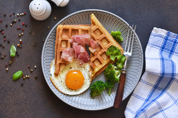 Belgian waffles for breakfast with egg, prosciutto and broccoli on a dark background.